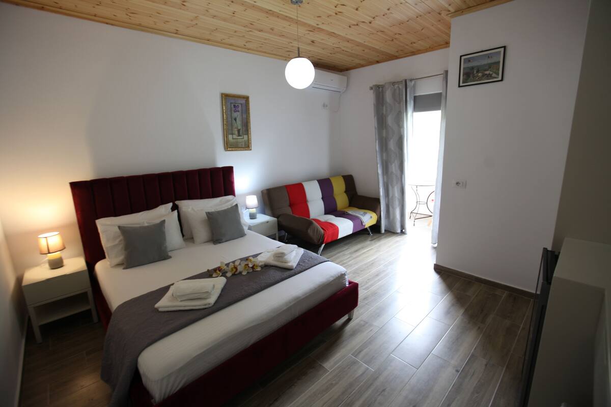 Un dormitorio con una cama grande, una mesita de noche con lámpara, un sofá y una ventana con cortinas.