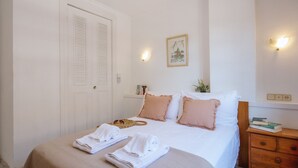 A neatly made bed with white and pink pillows, a bedside table with books, and a wall-mounted light fixture. - Avalon (Javea / Xàbia)