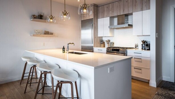 A modern kitchen with a large island, white cabinetry, stainless steel appliances, and pendant lighting.