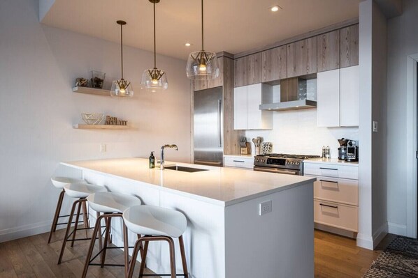 A modern kitchen with a large island, white cabinetry, stainless steel appliances, and pendant lighting.