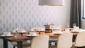A dining area with a wooden table set for six, a large pot on the stove, and a patterned wallpaper background.