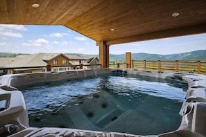 A hot tub with a wooden deck and a view of a house and mountains.