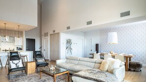 A spacious living area with a sofa, armchairs, and a coffee table. A dining table with chairs is visible in the background.