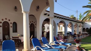 A covered outdoor area with blue lounge chairs, a table, and potted plants. - Villa Balneari Resort. Vacaciones en Familia y amigos Piscina Tenis Golf, Futbol (Rustical Balneario. Mont-roig del Camp)