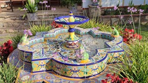 A colorful fountain with intricate tile work, surrounded by various plants and flowers. - Villa Balneari Resort. Vacaciones en Familia y amigos Piscina Tenis Golf, Futbol (Rustical Balneario. Mont-roig del Camp)