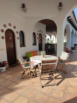 An outdoor patio with a round table and wooden chairs, surrounded by arches and potted plants.