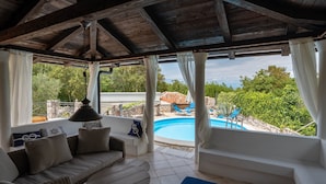 A covered outdoor seating area with a pool view, wicker furniture, and a ceiling fan. - Villa Nana (Dobrinj)