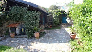 A stone pathway leading to a rustic building with a blue door, surrounded by lush greenery and potted plants. - Villa Nana (Dobrinj)