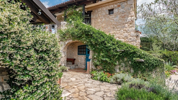 A stone building with a covered entrance, a stone pathway, and lush greenery. - Villa Nana (Dobrinj)