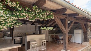 A rustic kitchen with a stone wall, wooden beams, a tiled floor, a built-in oven, a refrigerator, and a bar area with stools. - Villa Nana (Dobrinj)