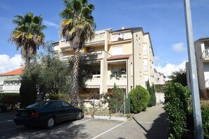 A multi-story residential building with balconies, a parked car, and surrounding greenery. - Apartment Emina (Sv. Filip i Jakov)