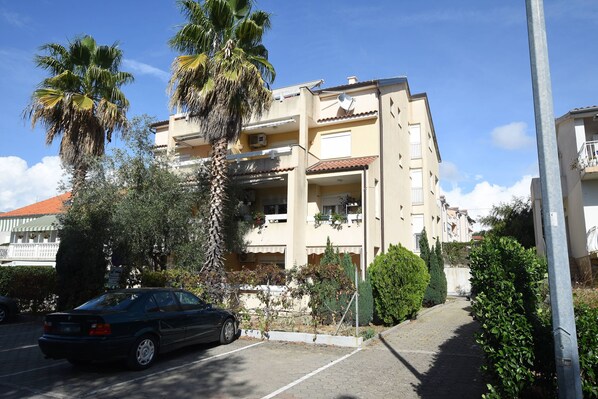 A multi-story residential building with balconies, a parked car, and surrounding greenery. - Apartment Emina (Sv. Filip i Jakov)