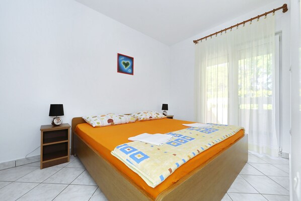 A bedroom with a bed, a nightstand, a lamp, a picture on the wall, and a window with curtains. - Apartment Emina (Sv. Filip i Jakov)