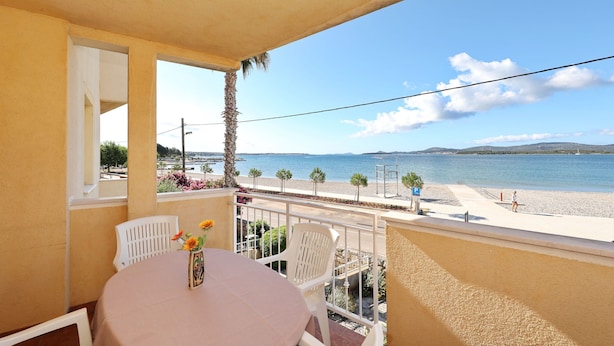 Ein Balkon mit Tisch und Stühlen, der Blick auf einen Strand und das Meer bietet.