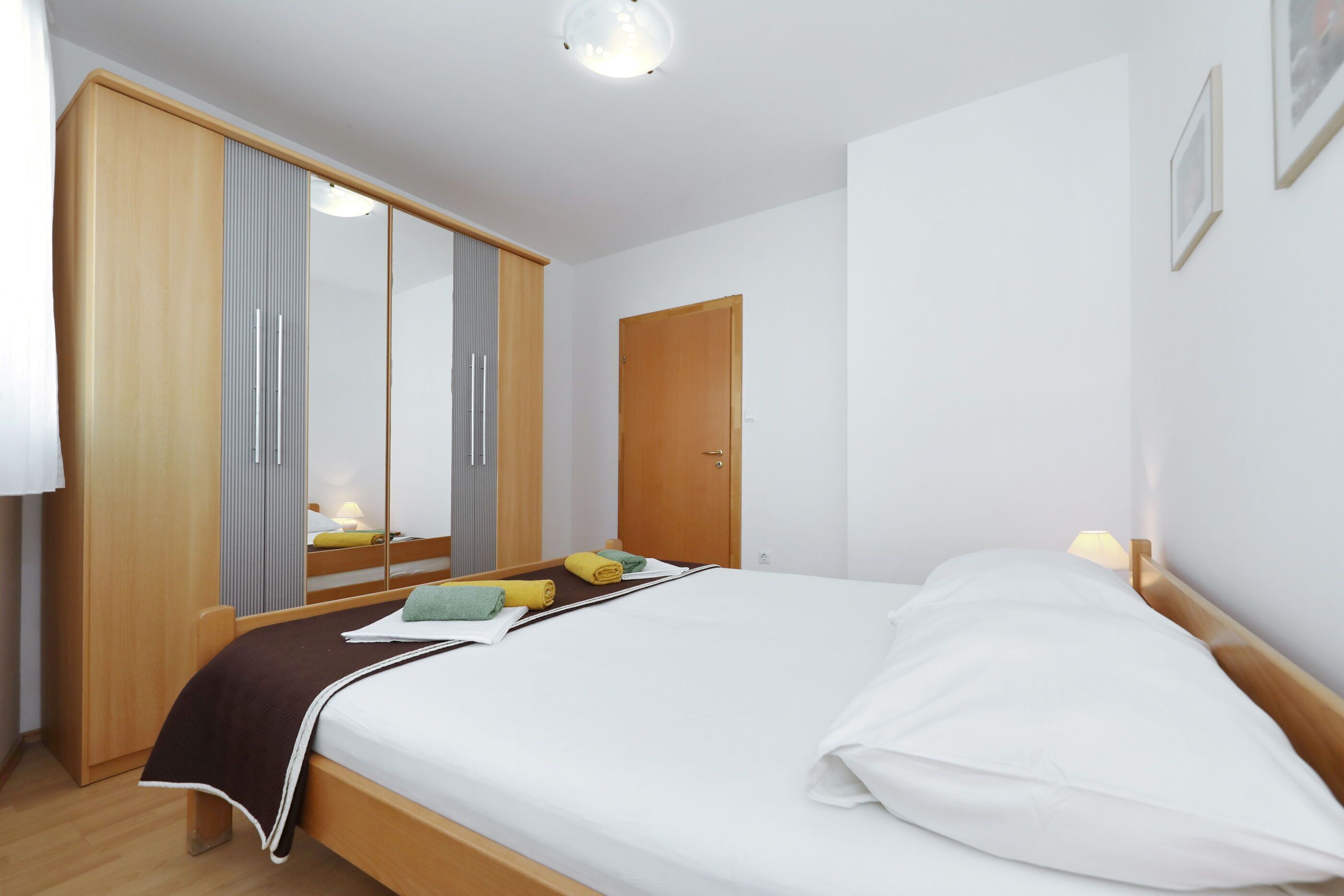 A bedroom with a bed, wooden wardrobe, and a mirror.