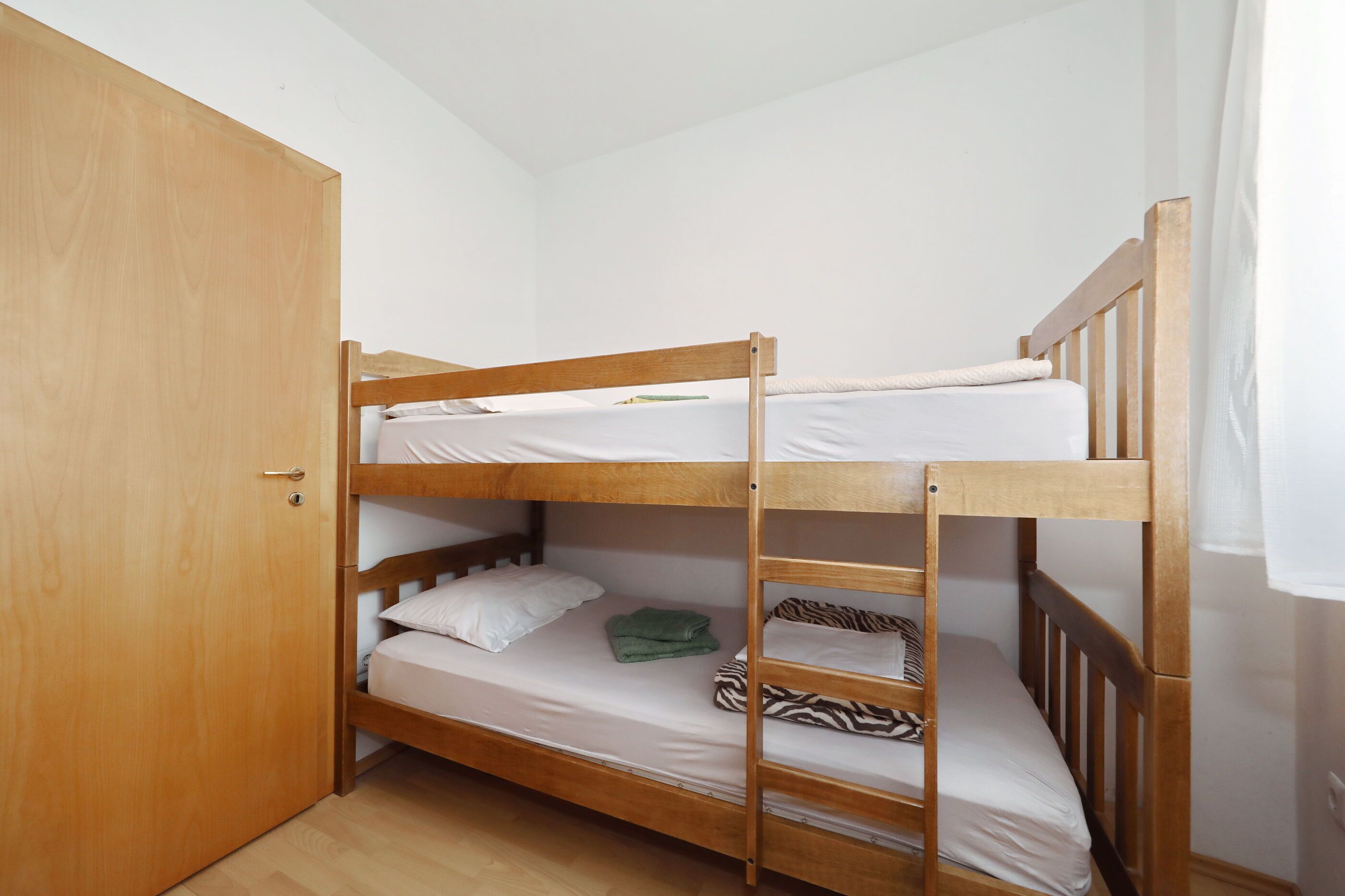 A bunk bed room with a wooden door, a lower bunk with a green towel, and a zebra-patterned pillow.
