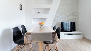 A dining area with a wooden table, black chairs, a TV on a white stand, and a stone-patterned wall. - Apartment Marica (Supetarska Draga)