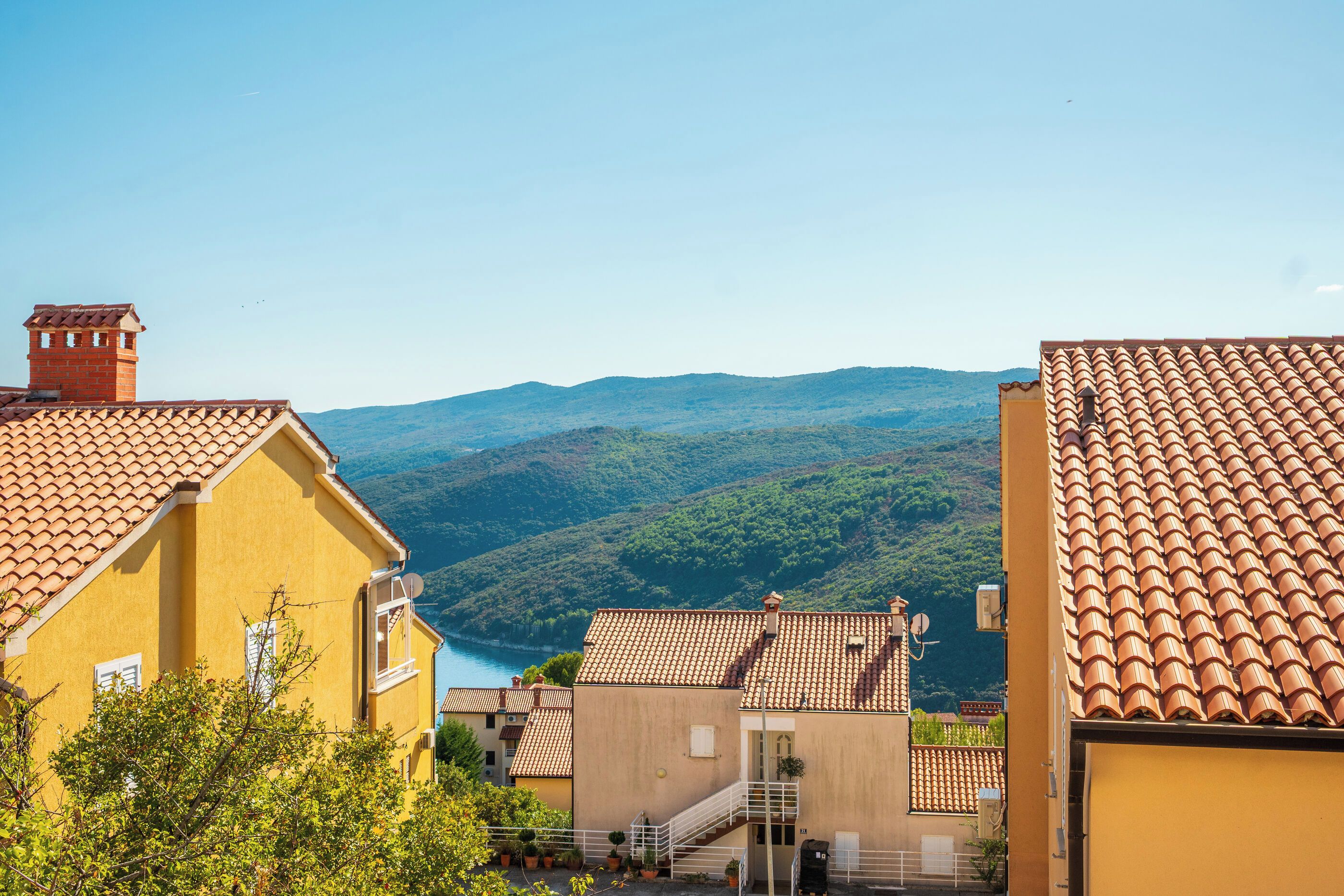 A yellow building with a red-tiled roof, a staircase, and a view of a valley.