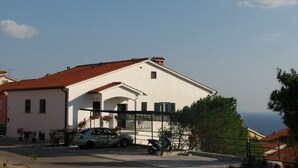 A white building with a red roof, a parked car, and a motorcycle in front. - Apartments Iris (Rabac)