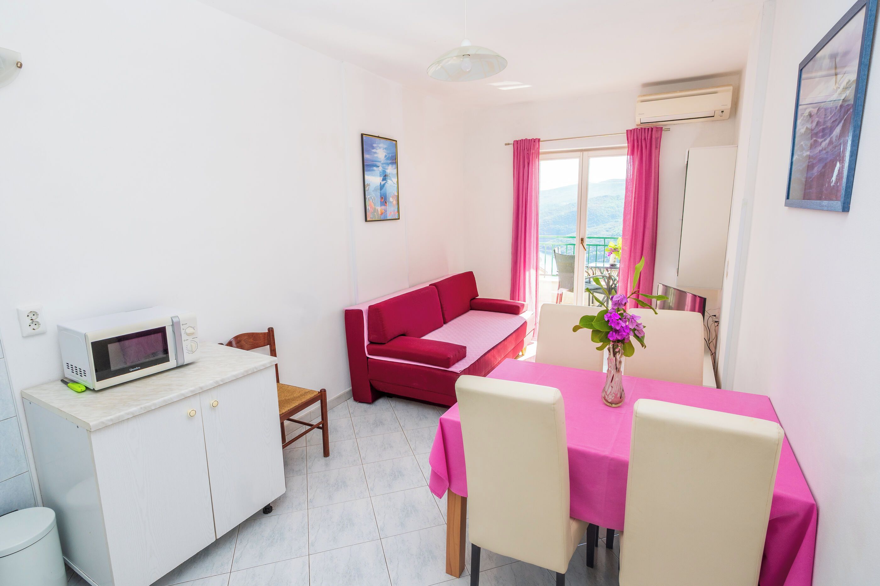 A compact living space with a kitchenette, a dining area, a sofa, and a balcony with a view.