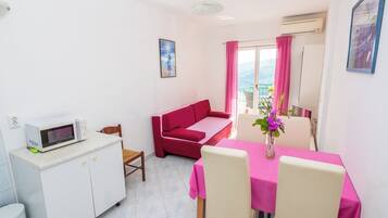A compact living space with a kitchenette, a dining area, a sofa, and a balcony with a view.