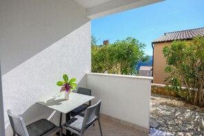 A balcony with a table and chairs, a potted plant, and a view of a building and trees.