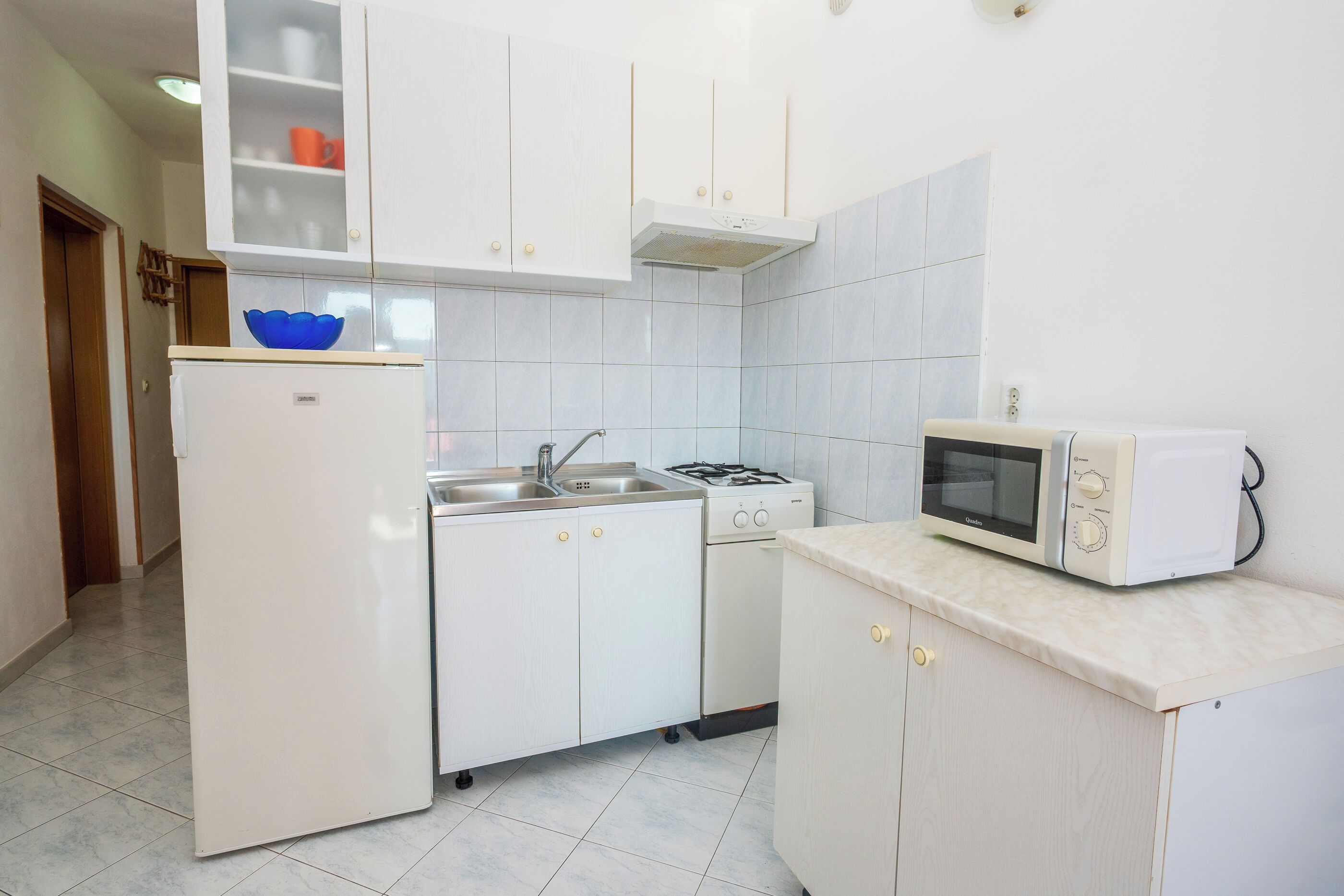 A compact kitchen with white cabinets, a refrigerator, a stove, a sink, and a microwave.
