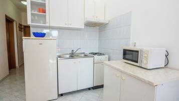 A compact kitchen with white cabinets, a refrigerator, a stove, a sink, and a microwave.