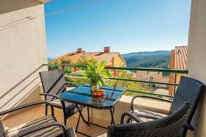 A balcony with wicker chairs, a glass table, and a potted plant.