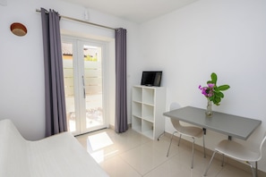 A room with a bed, a desk with a chair, a television, and a plant.