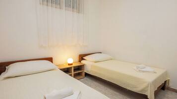 A room with two single beds, a bedside table with a lamp, and a window with sheer curtains.