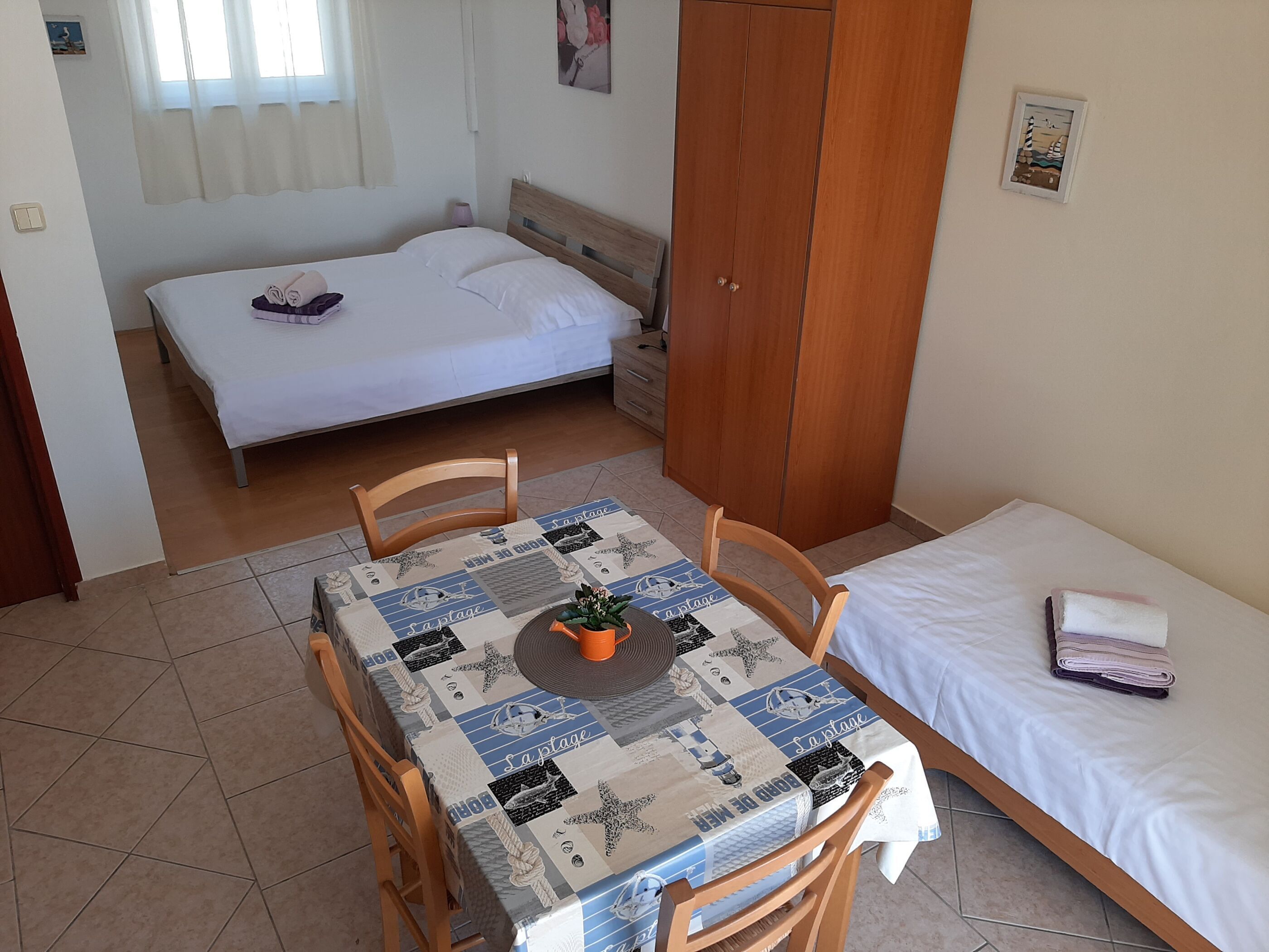 Ein kleiner, ordentlicher Raum mit einem Bett, einem Tisch mit Tischdecke und einem Kleiderschrank.