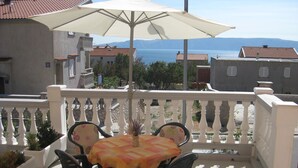 A balcony with a table and chairs, a large umbrella, and a view of the sea. - Apartments Pavelic (Povile)