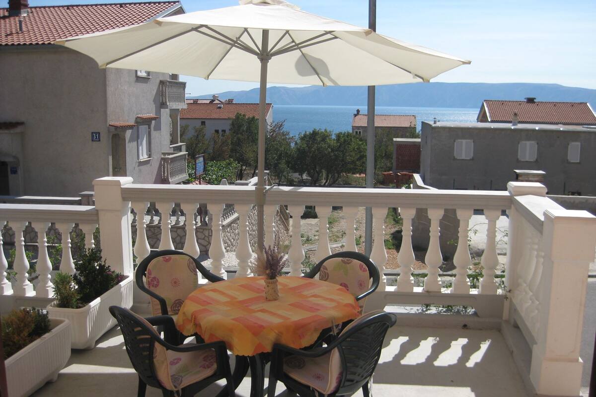 Un balcon avec une table et des chaises, un grand parasol et une vue sur la mer.