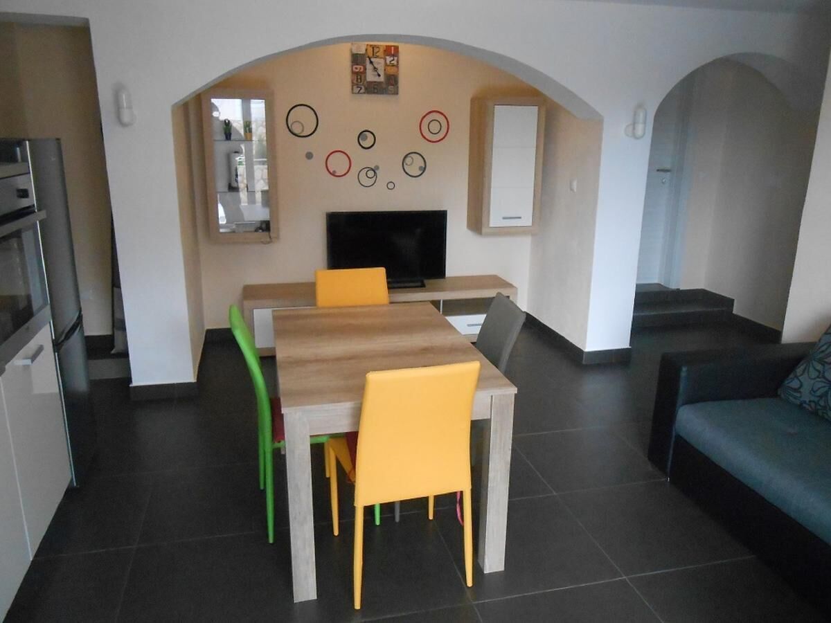 A modern kitchen with a dining area, a flat-screen TV, and a staircase leading to another level.