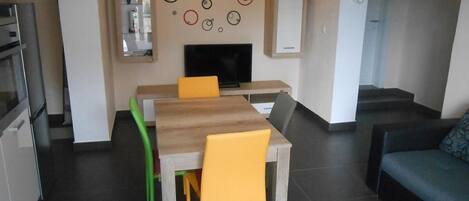 A modern kitchen with a dining area, a flat-screen TV, and a staircase leading to another level.