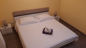 A neatly made bed with white linens, two bedside tables with lamps, and a folded towel on the bed. - Apartments Pavelic (Povile)