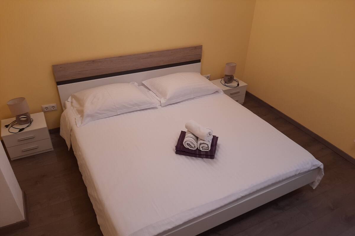 Un lit bien fait, avec du linge de lit blanc, deux tables de chevet avec des lampes et une serviette pliée posée sur le lit.