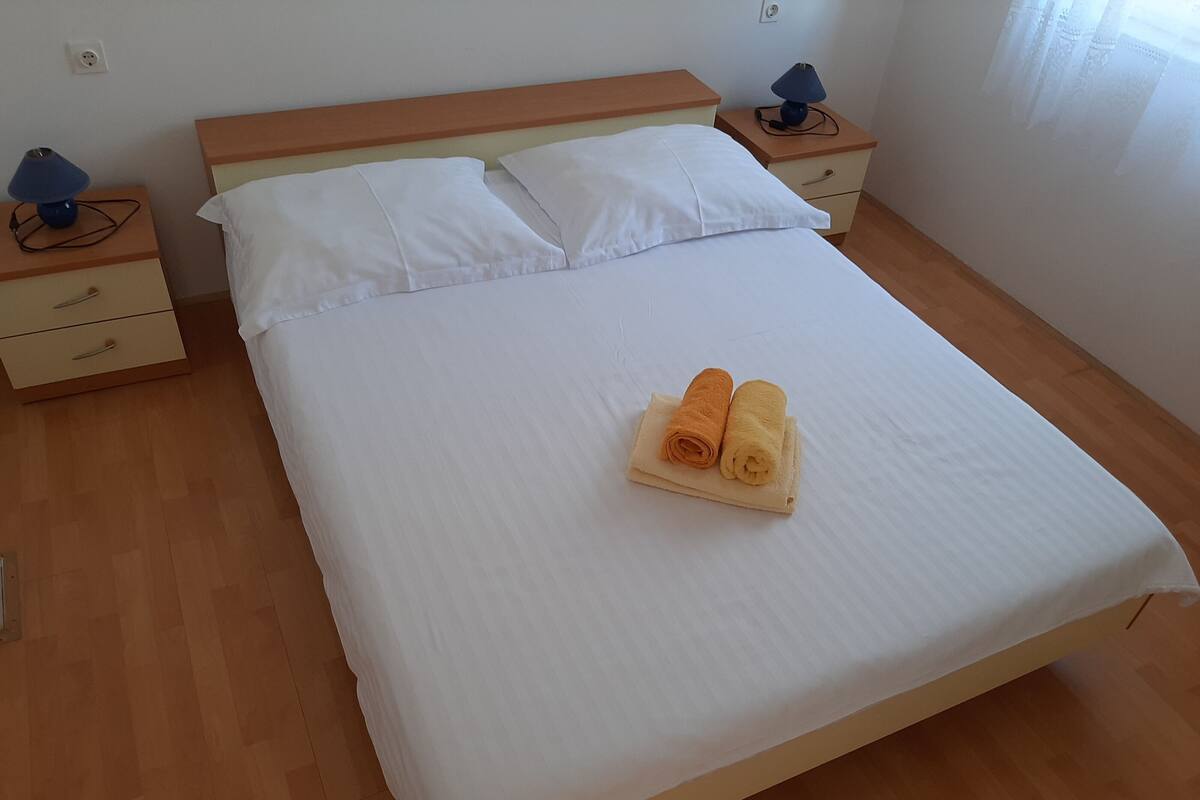 Un lit bien fait, avec des draps blancs et deux serviettes enroulées posées sur le lit.