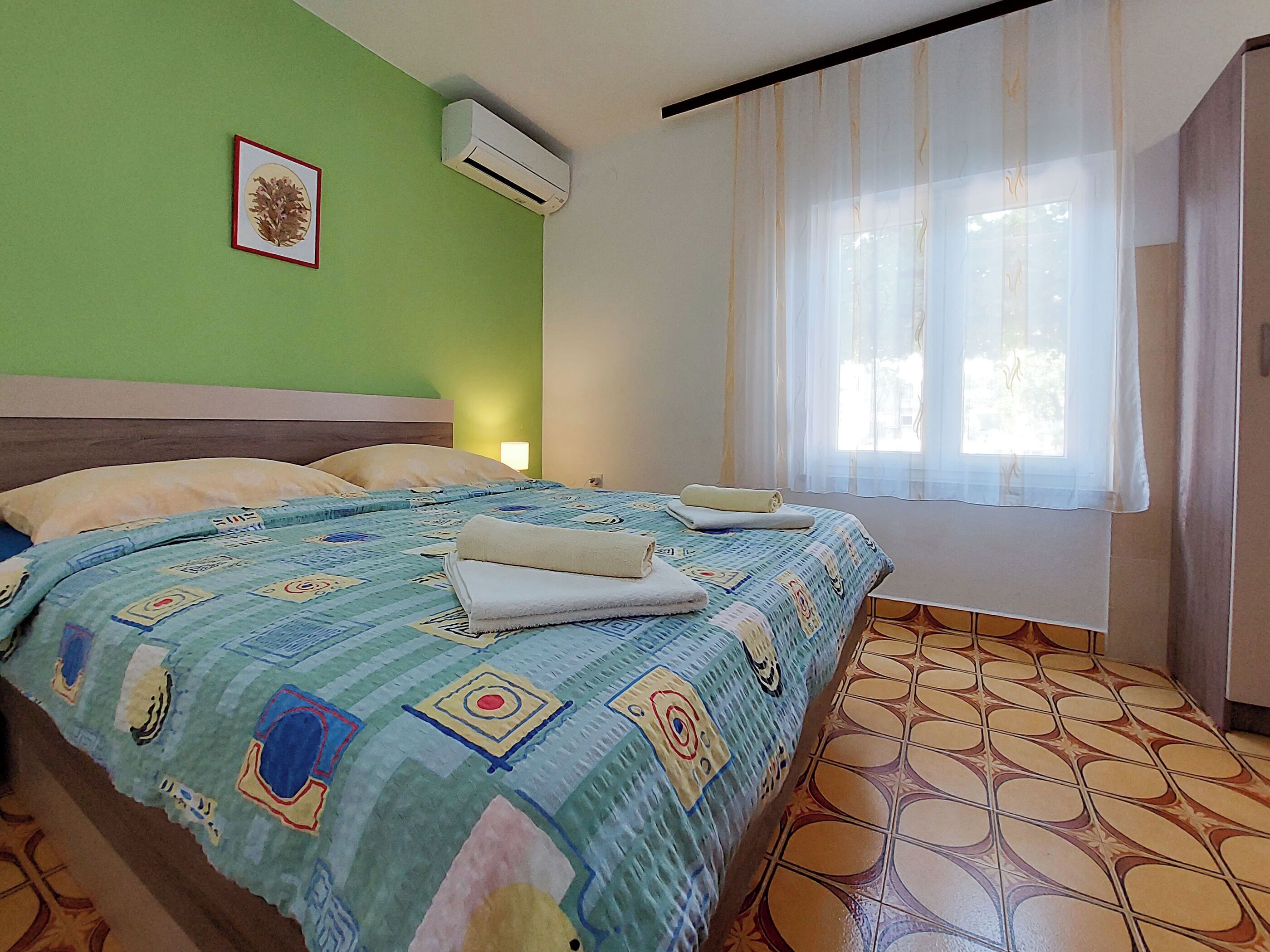 A hotel room with a bed, a window with curtains, and a wall-mounted air conditioner.
