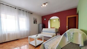 Ein Wohnzimmer mit Sofa, Couchtisch, Esstisch mit Stühlen und einer Küche im Hintergrund.