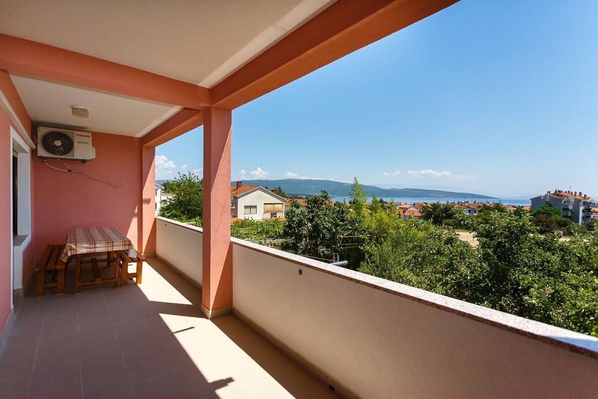 A balcony with a table and chairs, overlooking a residential area with houses and a clear sky.