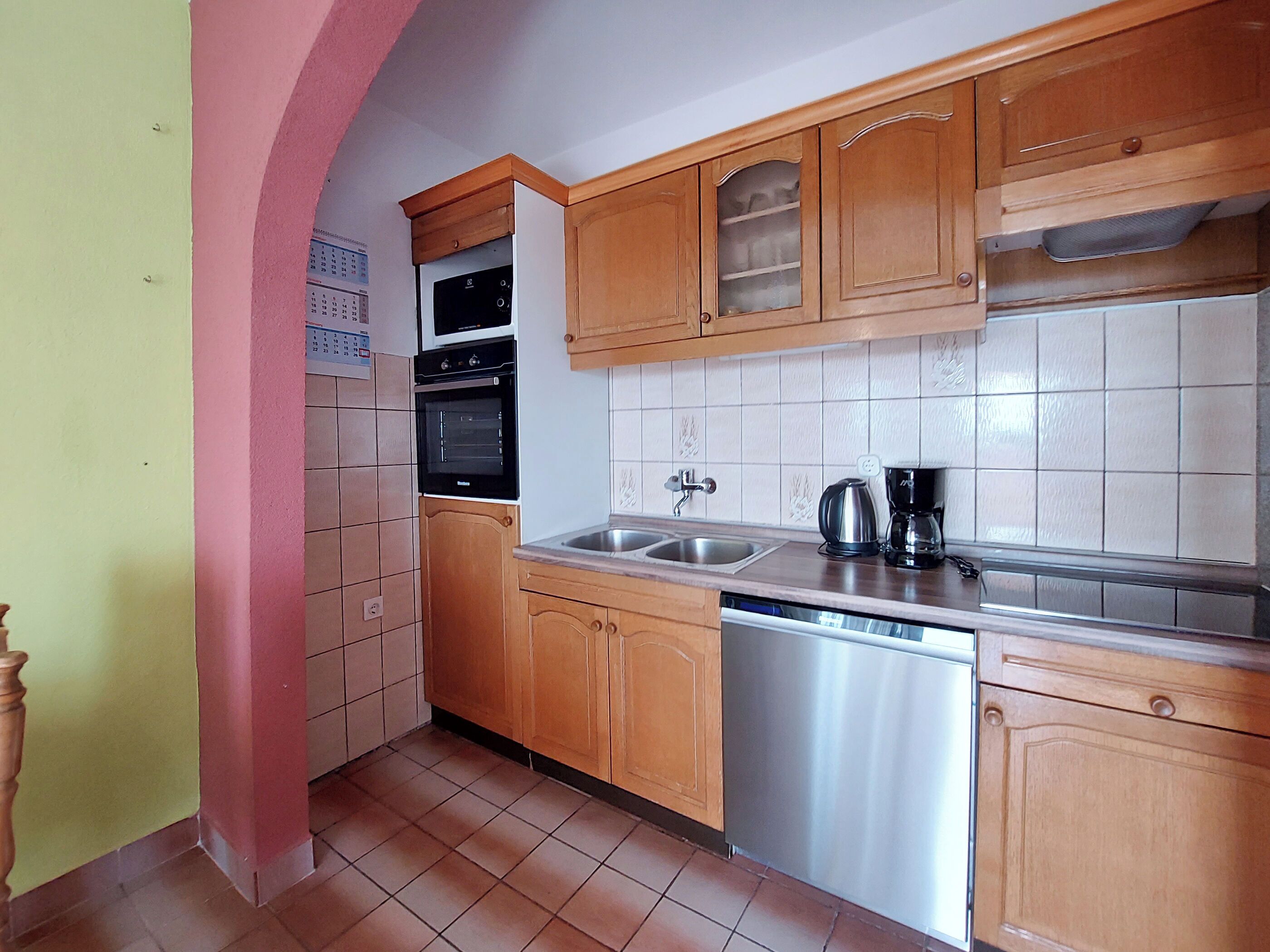 A compact kitchen with wooden cabinets, a dishwasher, a double oven, and a coffee maker.