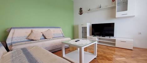 A living room with a sofa, a coffee table, a flat-screen TV, and a white cabinet with shelves.