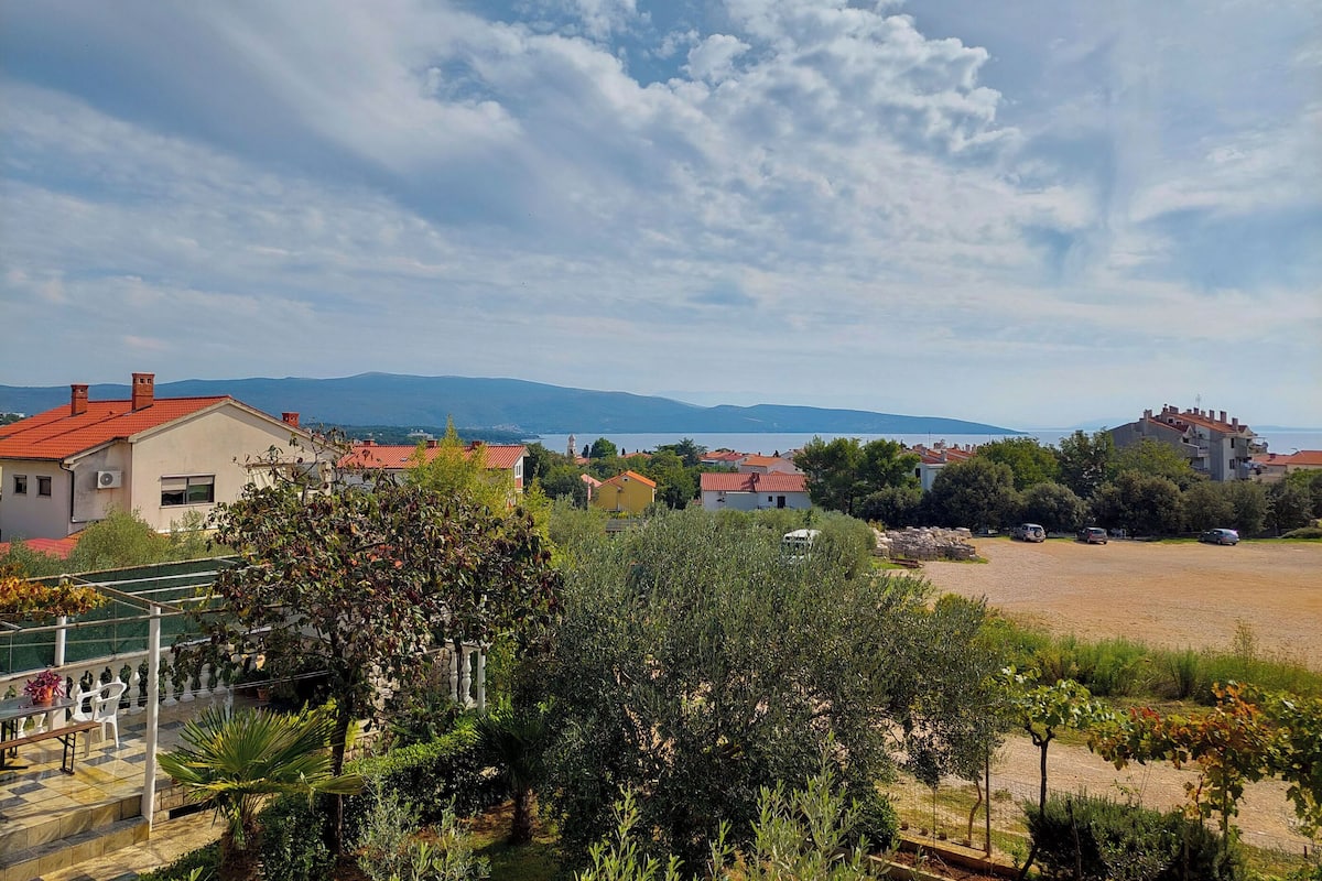 A residential area with houses, a garden, and a view of the sea and mountains.