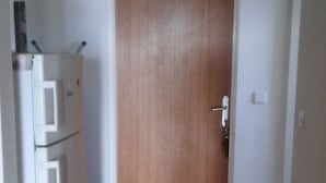 A hallway with a wooden door, a white refrigerator, and a small rug on the floor. - Apartment Andela (Senj)