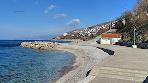 A coastal promenade with a pebble beach, a stone breakwater, and hillside buildings. - Apartment Andela (Senj)