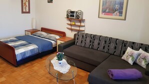 A room with a bed, a sofa, a small round table with a plant, and a shelf with audio equipment. - Apartment Andela (Senj)