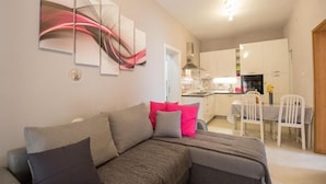 Una sala de estar moderna con un sofá gris, una mesa de comedor con sillas, y una cocina al fondo.