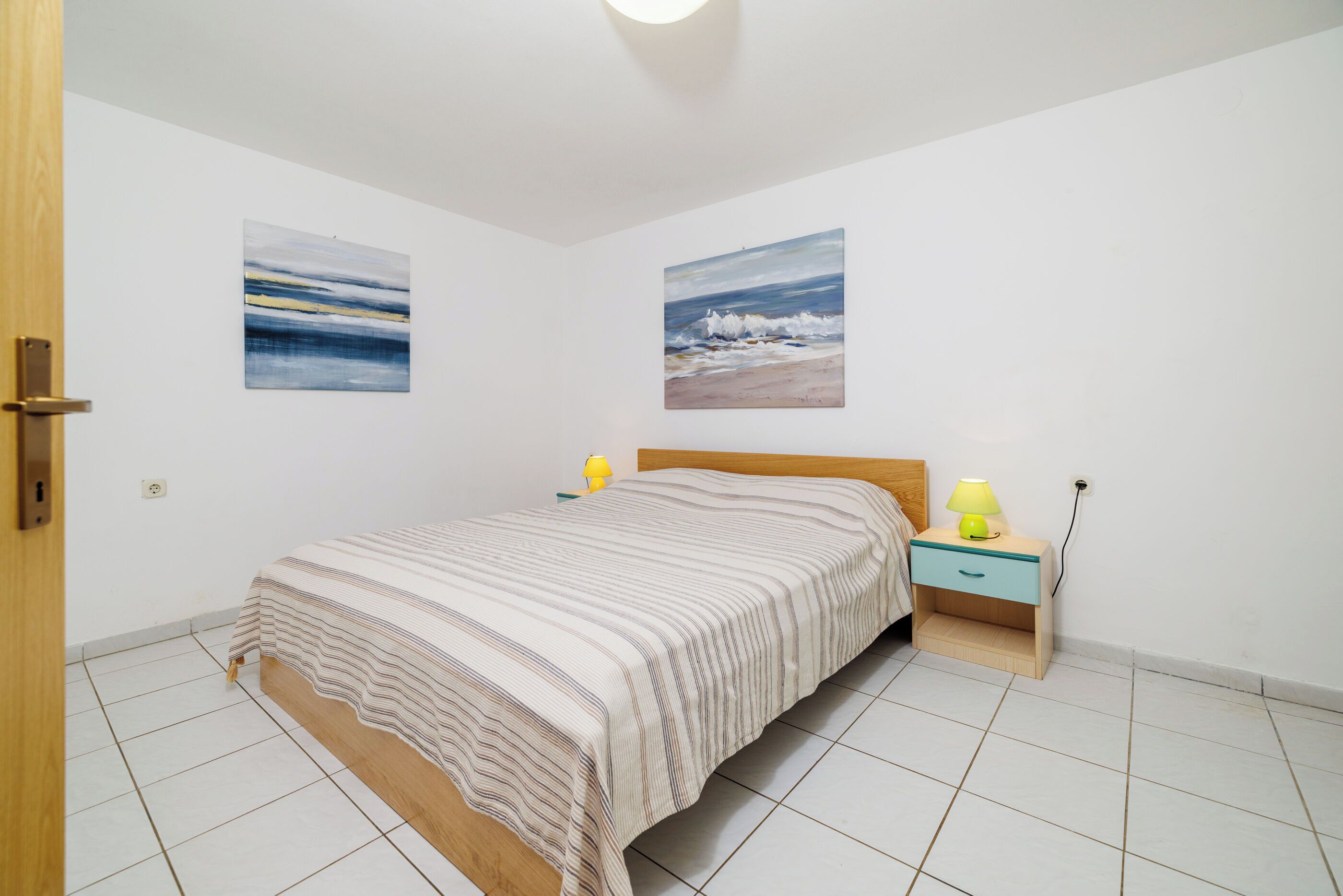 Une chambre à coucher comprenant un lit, une table de chevet, deux lampes fixées au mur et deux tableaux.